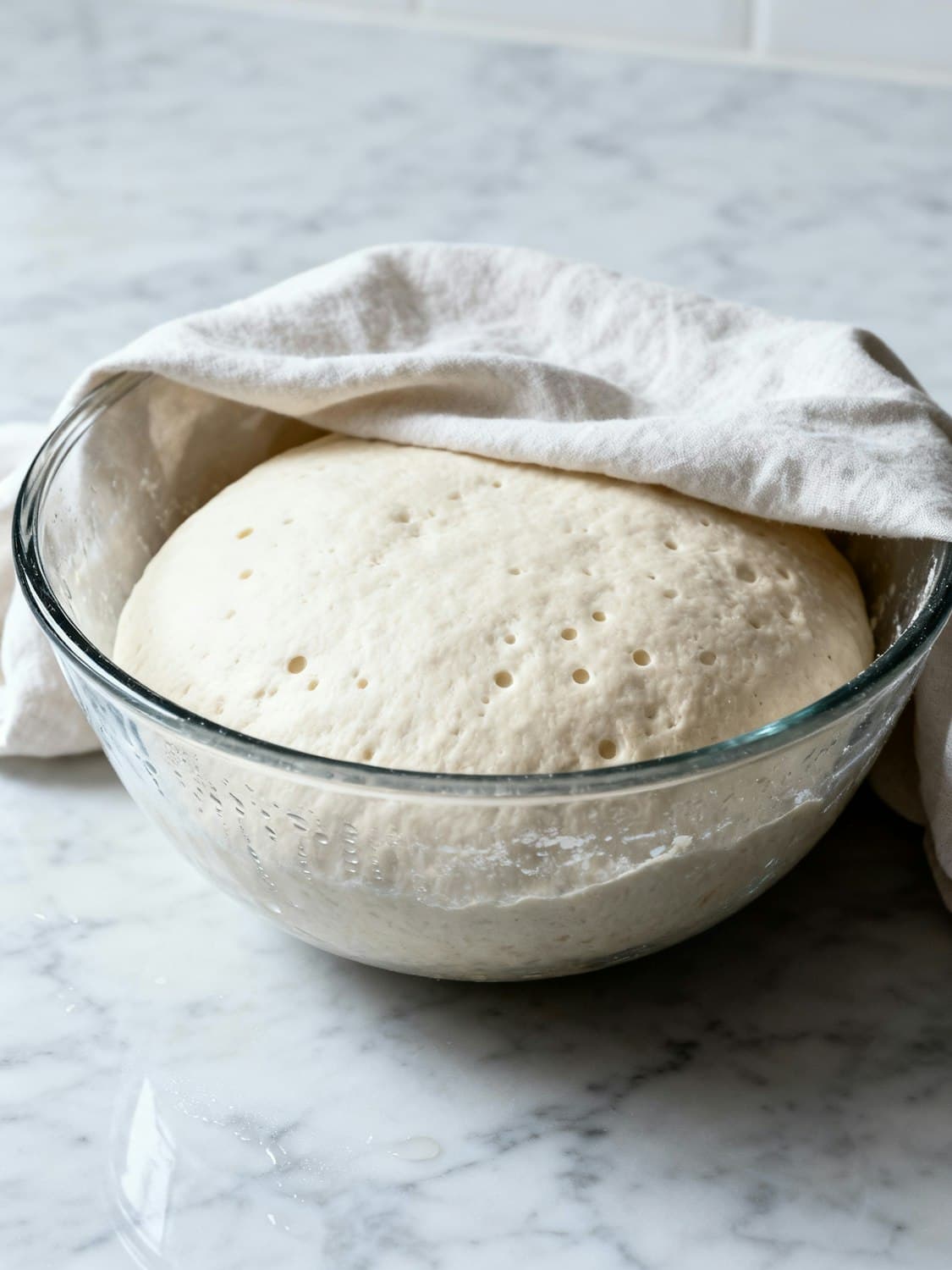 Dough rising slowly in a glass bowl under a linen cloth